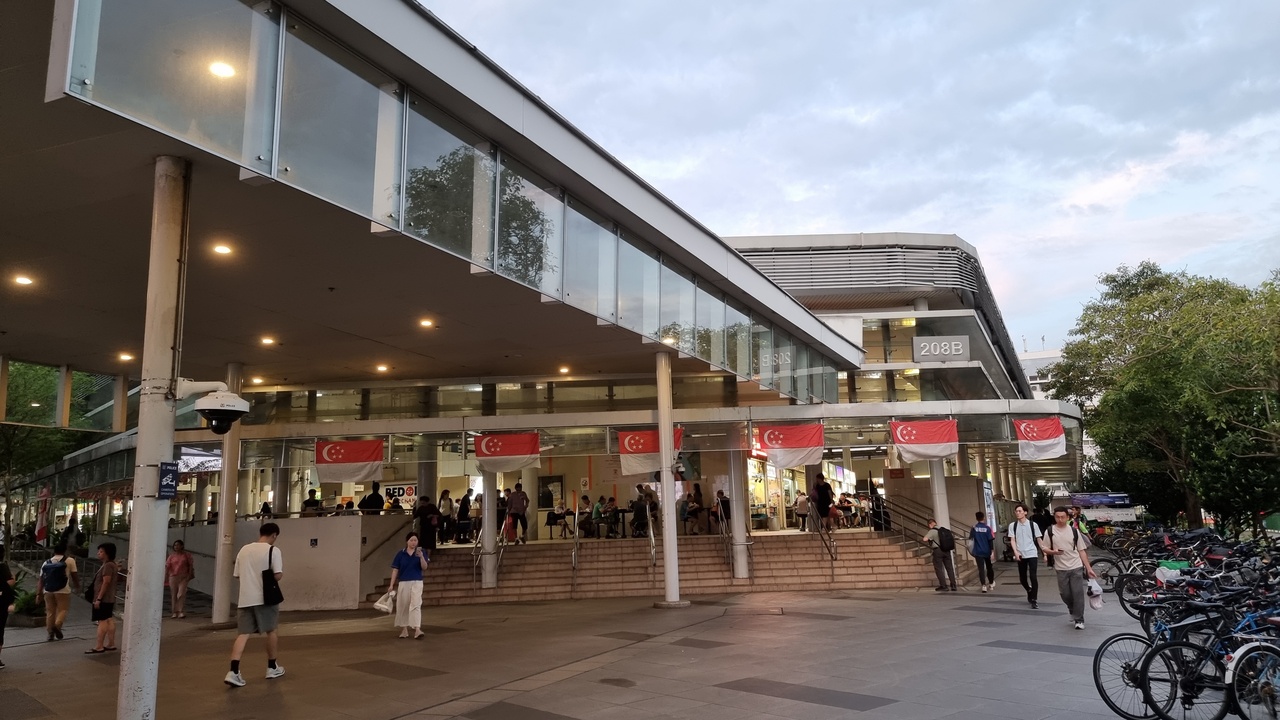 Busy hawker centre with a variety of food stalls and patrons eating at communal tables