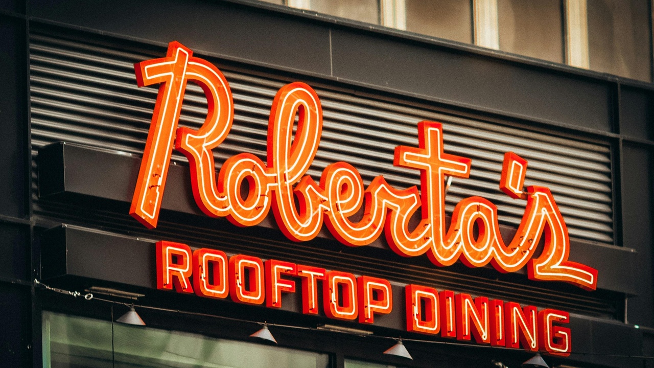 A bustling outdoor dining street at dusk with string lights, tables, and a view toward downtown Phoenix skyline.