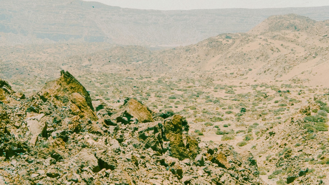Hikers walking a narrow trail in the Cal Madow mountains, with rocky peaks and juniper shrubs