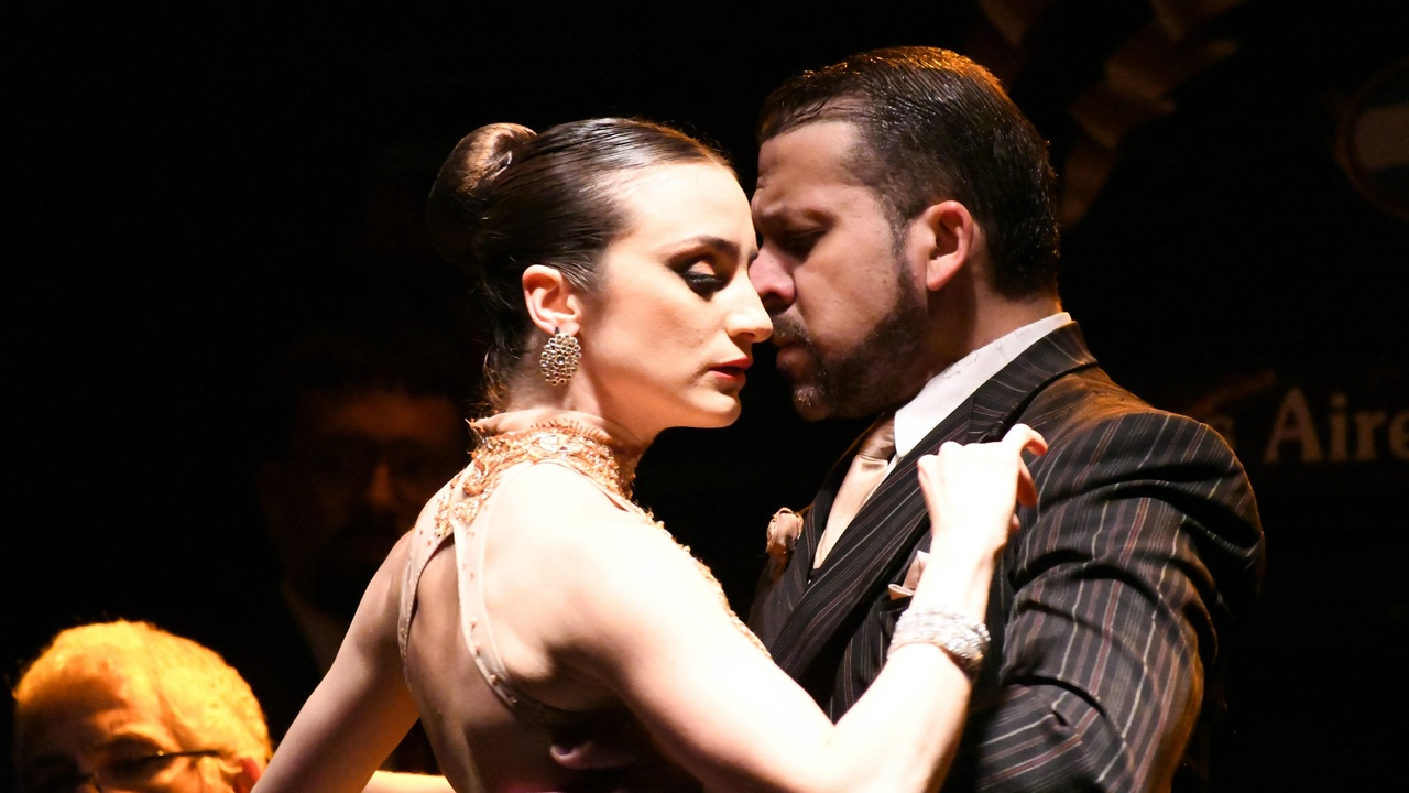 Locals dancing tango in a dimly lit milonga with bar seating and vintage décor.
