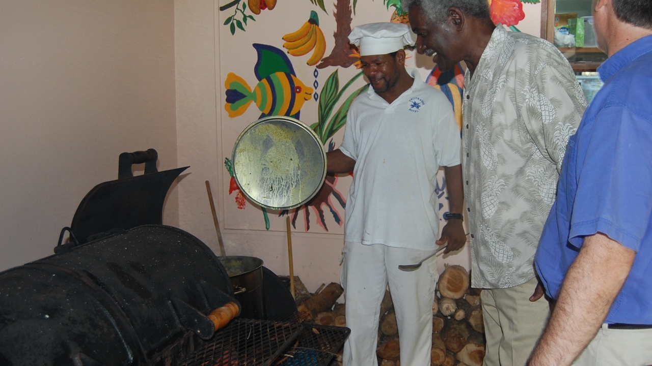 Communal cooking of Oil Down with large pots and people serving food