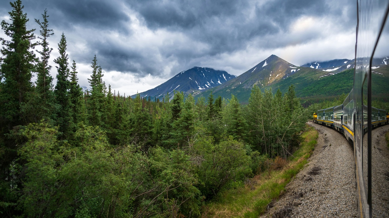 Alaska Railroad train crossing a mountain valley with snow-capped peaks in the distance