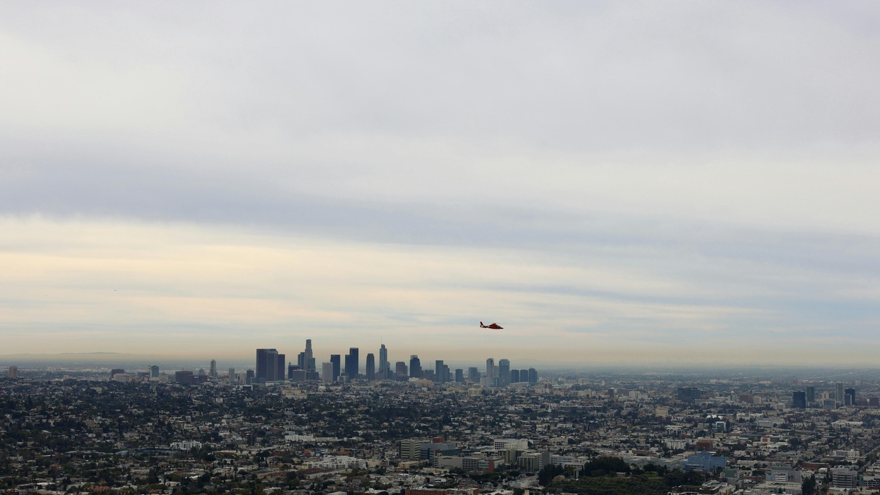 Helicopter flying over Los Angeles coastline and skyline at sunset