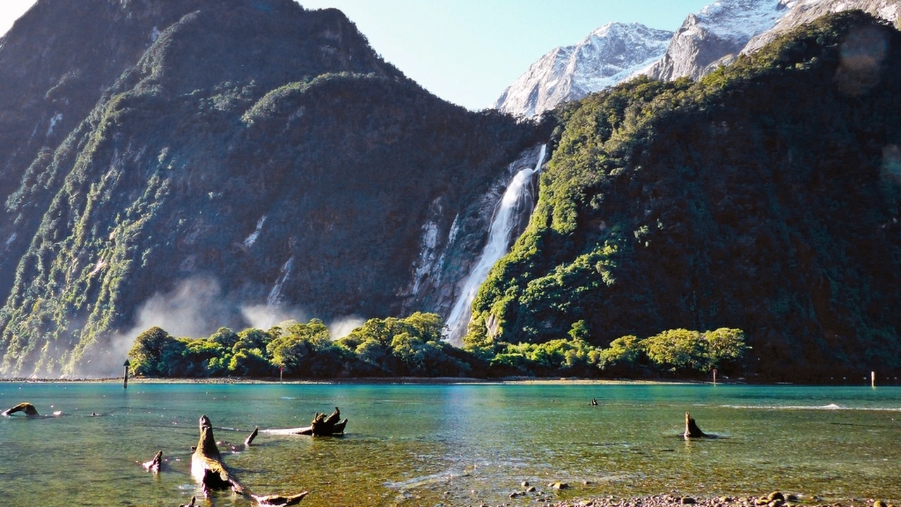 Snow-capped Southern Alps rising above a fiord with hikers on a coastal track; mountains, fiords and outdoor activities in New Zealand