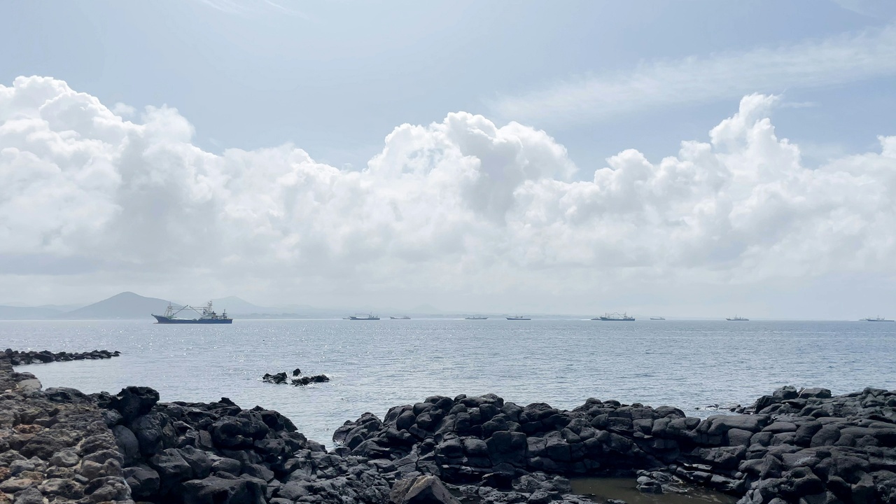 Scuba diver near Jeju volcanic reef with Haenyeo boats in distance