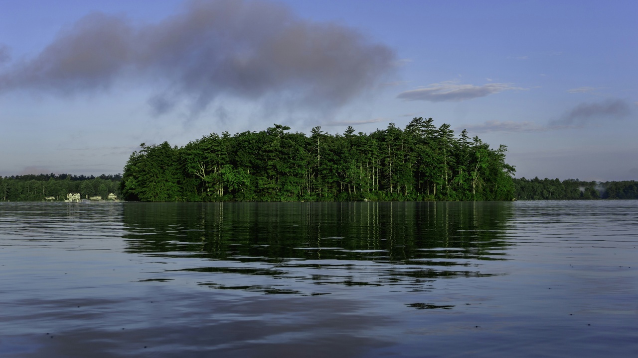 Paddlers on a calm New Hampshire lake with pine-lined shore and distant hills.