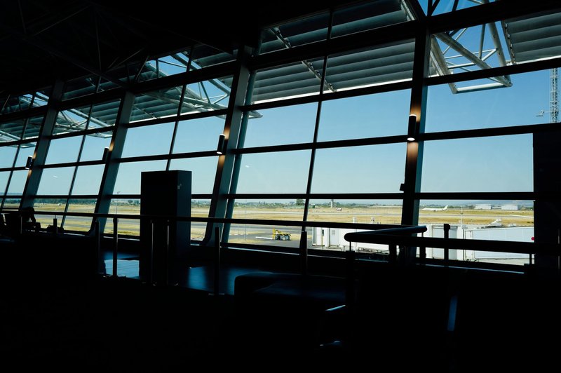 View from inside an airport terminal overlooking the runway under a bright blue sky.