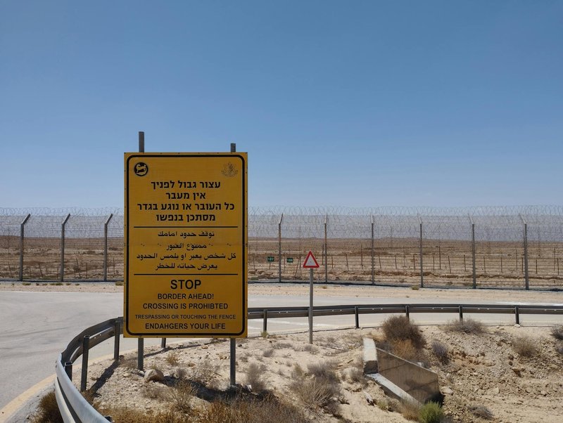 A warning sign prohibiting crossing near a desert border area with clear blue sky.
