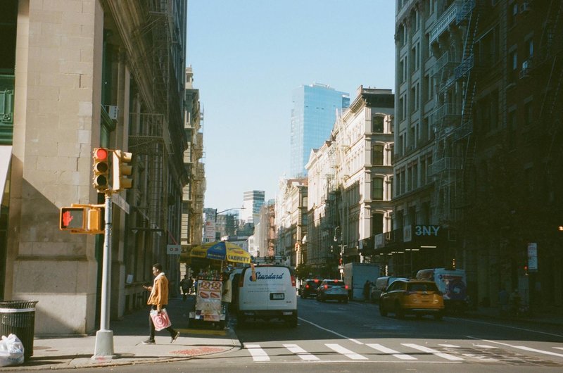 Busy urban street in New York City with people, vehicles, and skyscrapers under a clear sky.
