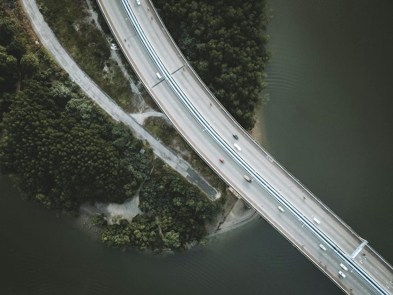 Drone shot capturing a highway curving over a river surrounded by lush green forest.