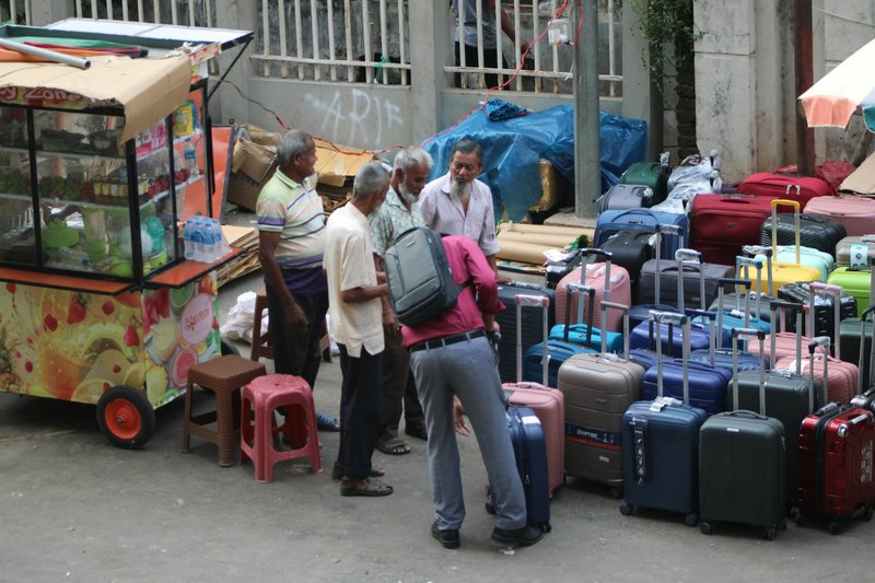 Vibrant street scene featuring people browsing colorful suitcases at an outdoor market stall.