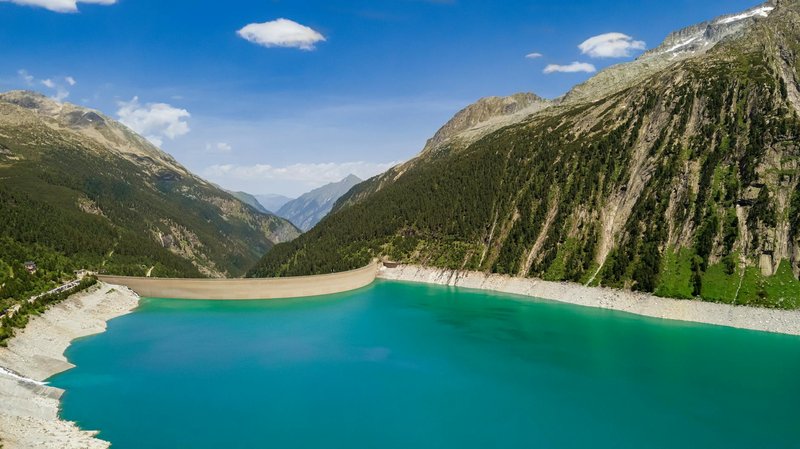 Stunning aerial shot of a dam and turquoise reservoir nestled in lush mountains.