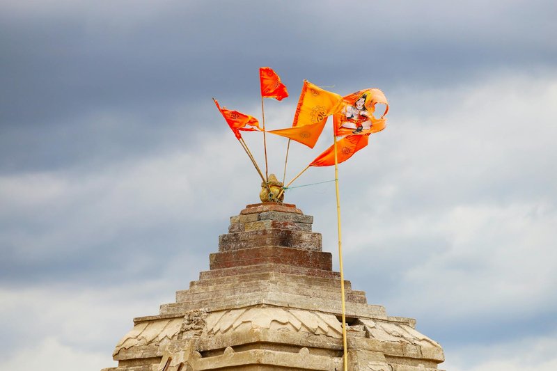 Vibrant orange flags adorn a historic temple roof under a dramatic cloudy sky.
