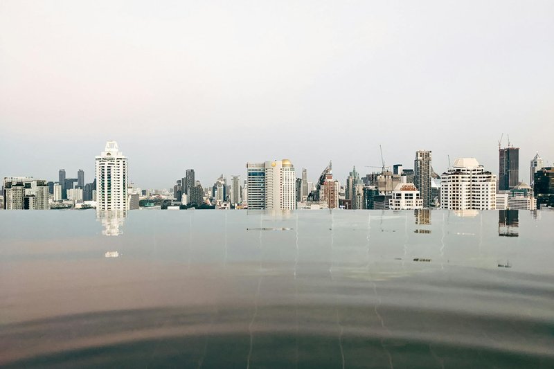 Tranquil infinity pool with reflections of the Bangkok skyline under a calm sky.