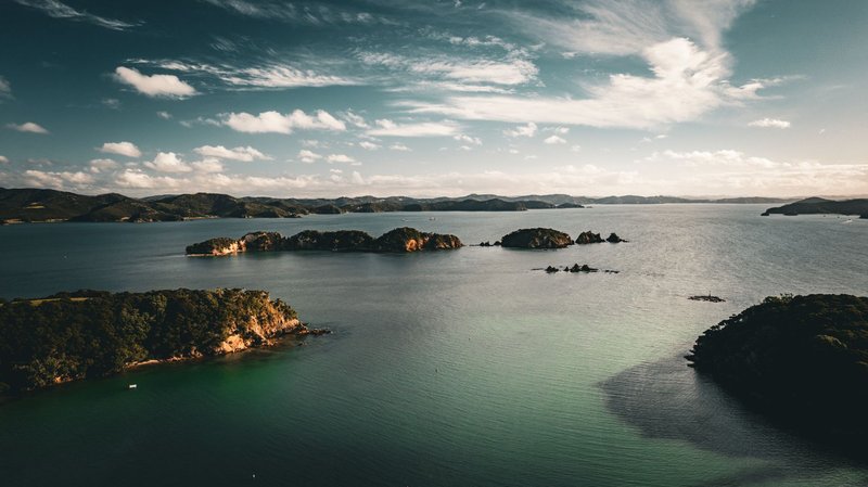 Stunning aerial shot of Northland's coastline, showcasing serene islands with clear waters and dramatic skies.
