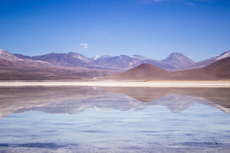 A breathtaking view of the serene Bolivian Altiplano lagoon with majestic mountains reflecting in the water.