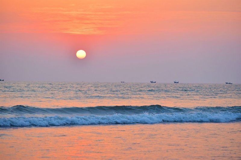 Tranquil sunset over Cox's Bazar beach with gentle waves and distant boats.