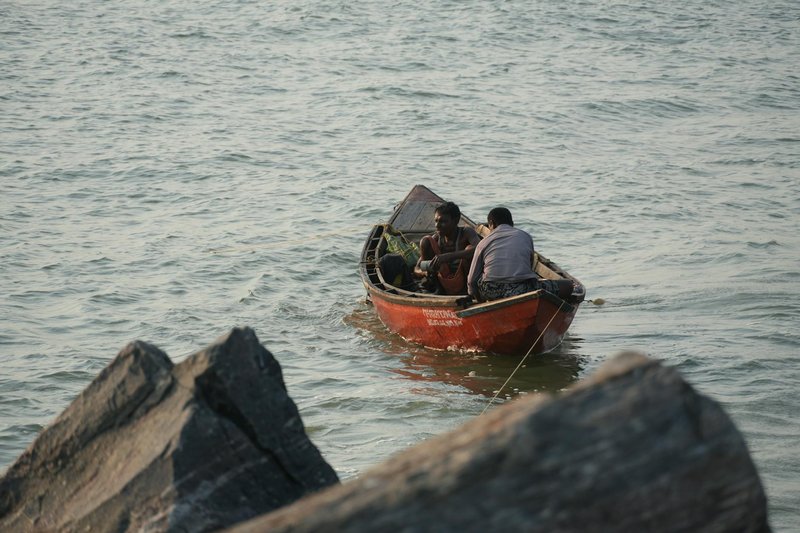 Fishermen steer a small red boat along the rocky coastline, capturing a serene seaside moment.