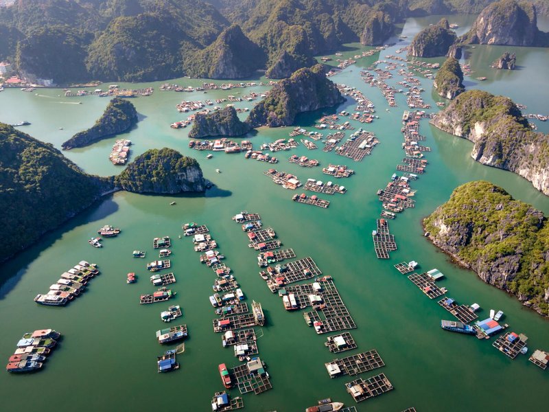 Stunning aerial view of floating villages amidst limestone islands in a serene green bay.