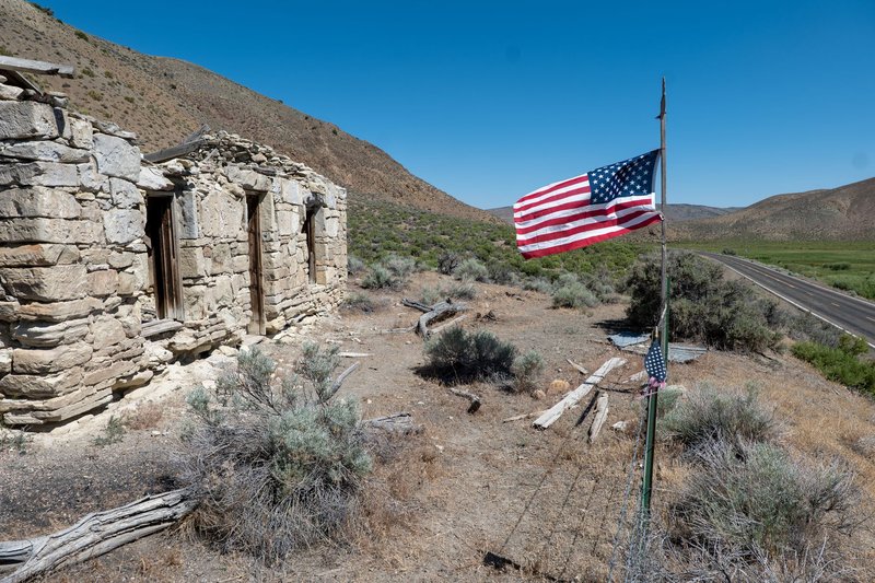 Rural landscape with an abandoned stone building and American flag under a clear blue sky.