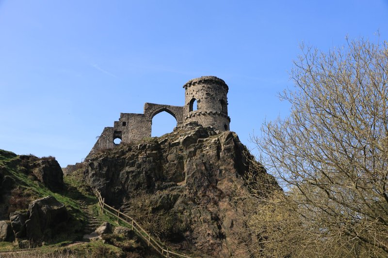Dramatic view of old castle remains atop a rocky hill in spring, captured under a clear blue sky.