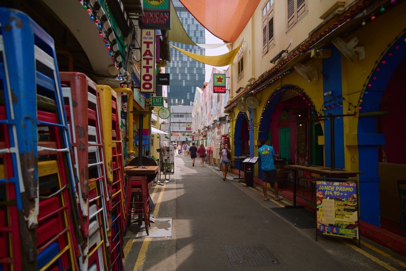 A vibrant, colorful alleyway filled with stacked chairs, shops, and people in an urban setting.