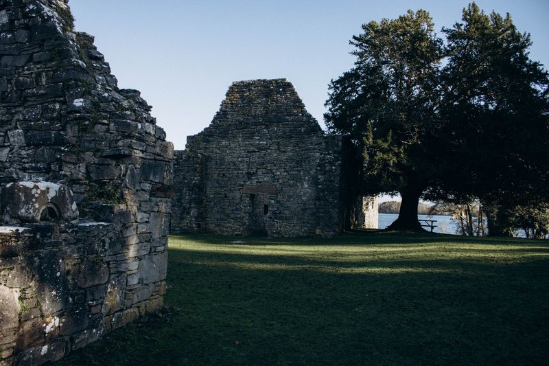 Explore the serene and ancient stone ruins of a monastery on Innisfallen Island, surrounded by lush greenery.