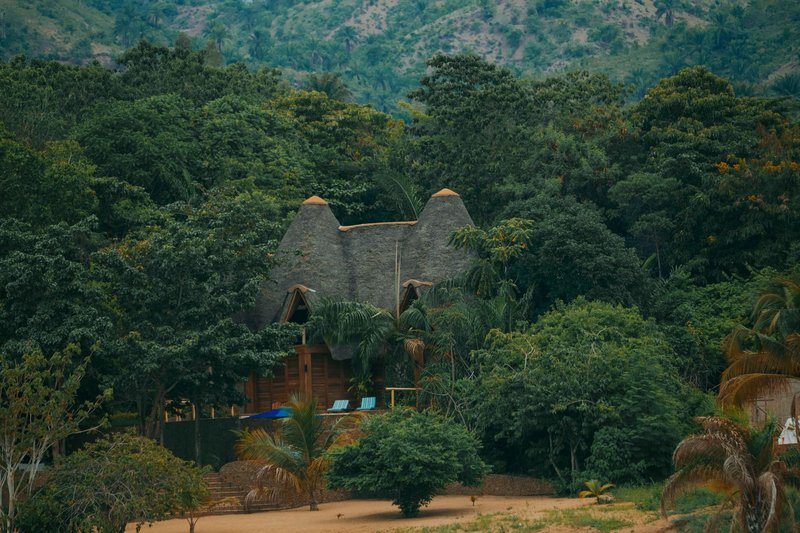 A rustic lodge with a thatched roof surrounded by lush greenery and hills.
