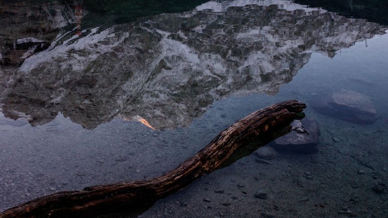 Serene mountain reflection in a calm lake with a weathered log in the foreground.