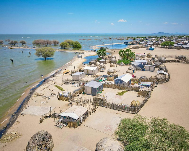A scenic aerial view of Kalokol village by Lake Turkana in Kenya, showcasing traditional huts and a vibrant landscape.