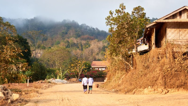 Two children walking on a rural dirt road in a peaceful village, Laos.