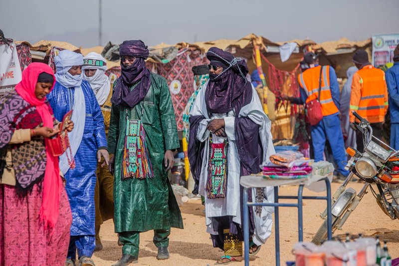 Vibrant scene at a desert market with Tuareg people in traditional attire, displaying culture and commerce.