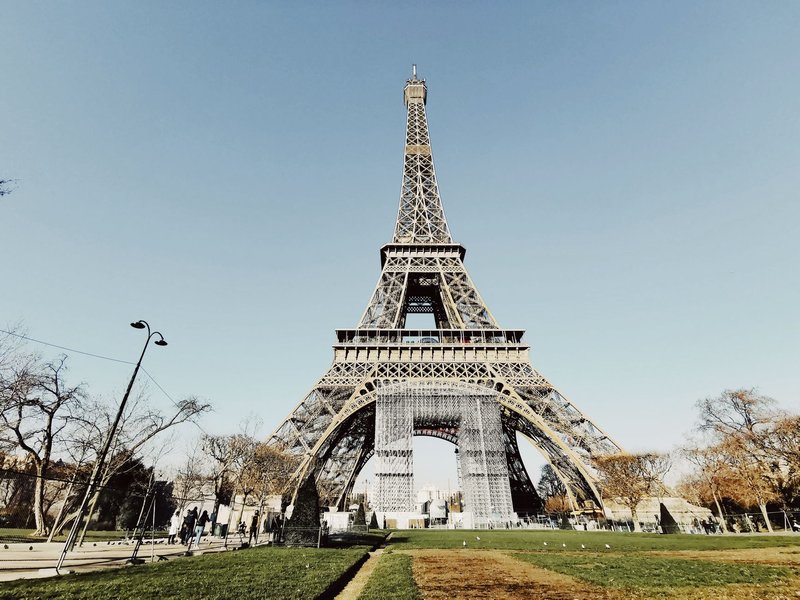 Low angle shot of the Eiffel Tower in Paris with blue sky and partial park view.