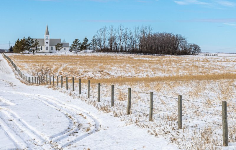 A serene winter landscape showcasing a rural church beside a snow-covered prairie in Saskatchewan, Canada.