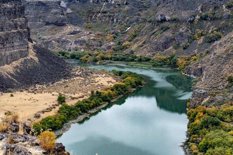 A stunning view of a tranquil river winding through a rocky canyon in autumn, showcasing vibrant foliage.