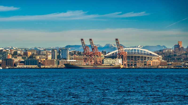 Seattle skyline featuring stadium and cranes by the waterfront on a clear day.