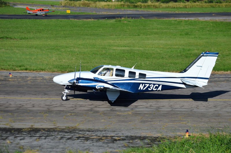 A small aircraft with registration N73CA taxiing on a sunny runway with green grass.