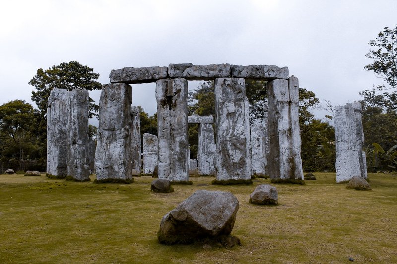 Replica stone structure resembling Stonehenge in a grassy outdoor setting with overcast skies.