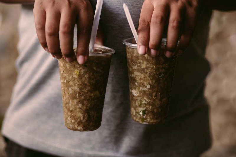Close-up of hands holding two iced drinks in plastic cups with straws, perfect for a hot day.