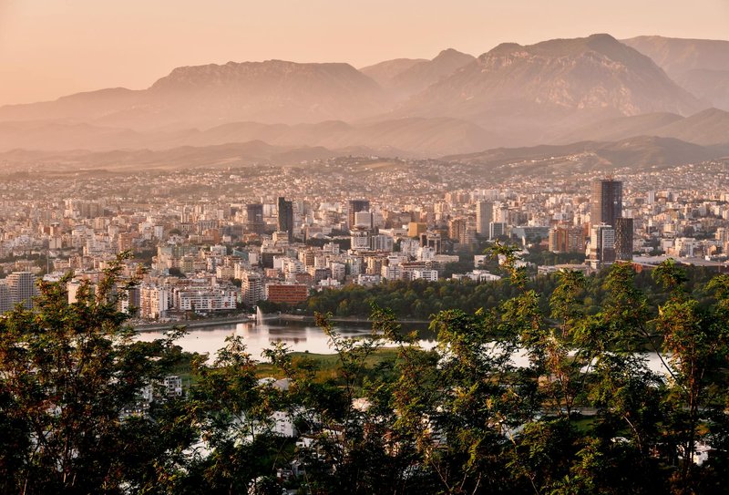 A stunning aerial view of Tirana's skyline framed by mountains and lush greenery during sunset.