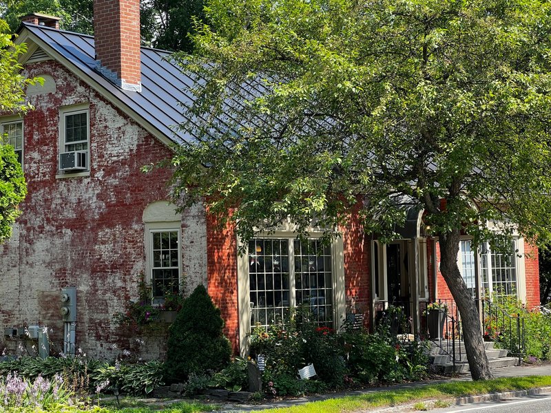 A picturesque rustic red brick house surrounded by summer greenery and vibrant plants.