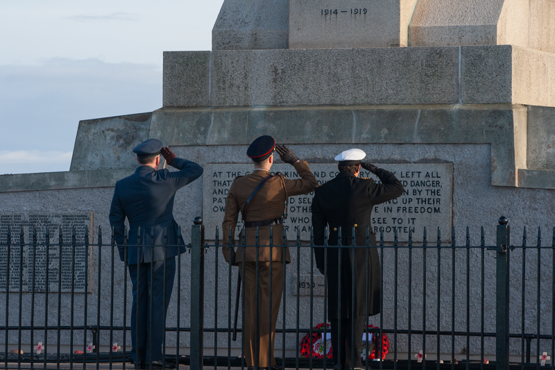 Three soldiers in uniform salute a World War I memorial, honoring fallen comrades.