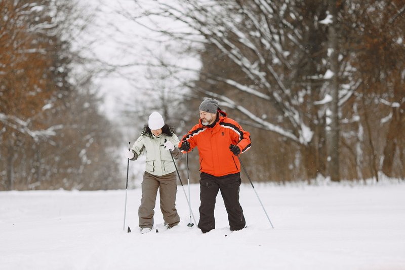 Happy couple skiing in a snowy winter landscape with trees in the background, wearing colorful jackets.