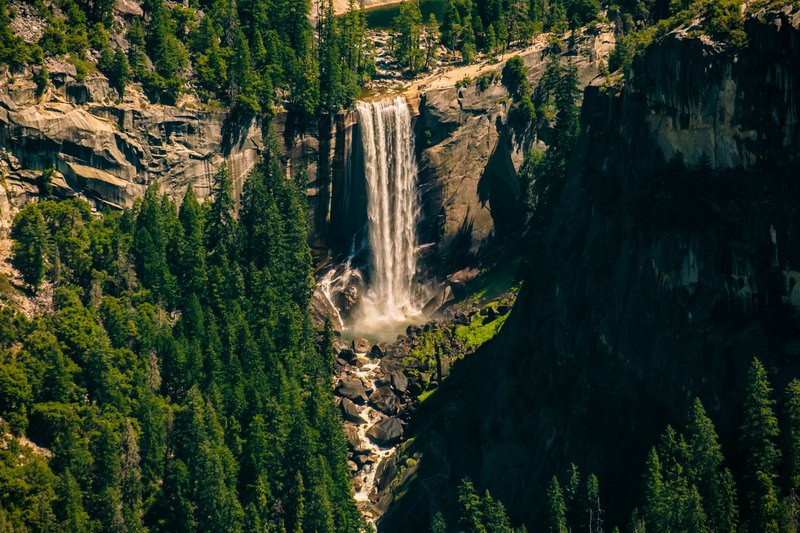 Stunning waterfall cascading down a cliff in Yosemite Valley, surrounded by lush greenery.