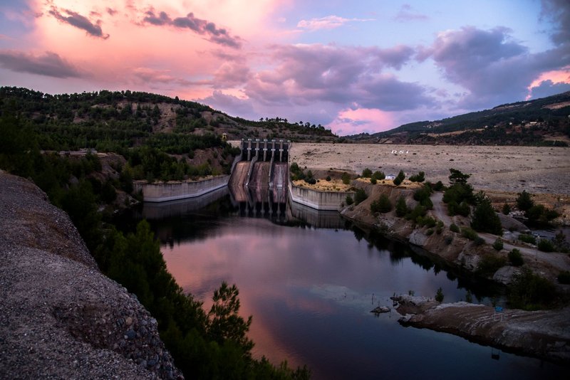 A breathtaking view of a dam and reservoir reflecting a colorful sunset sky.
