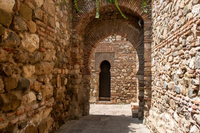 Sunlit stone arches in a historic passage, showcasing ancient architecture in Malaga, Spain.