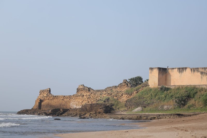 A scenic view of ancient ruins by the beach under a clear blue sky.