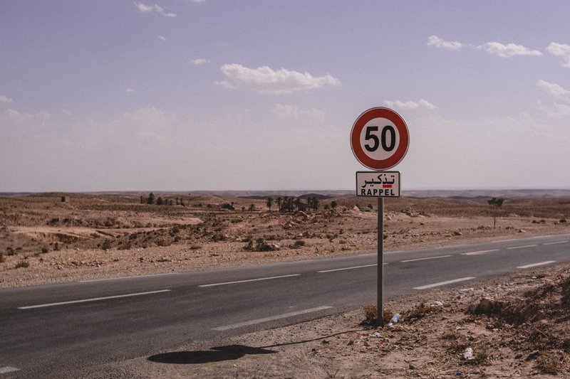 A deserted road in Tunisia marked with a 50 km/h speed limit sign under a clear sky.