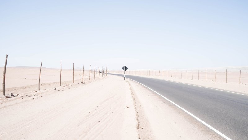 A deserted road winds through a vast, arid desert under a bright blue sky, capturing the essence of solitude and travel.