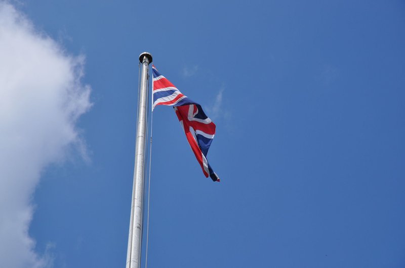 Union Jack flag waving on a flagpole against a clear blue sky in London, UK.
